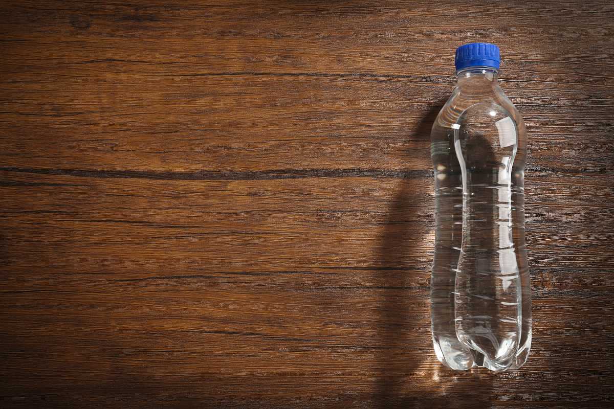 A clear bottle with distilled water and a blue cap is placed upright on a wooden surface. 