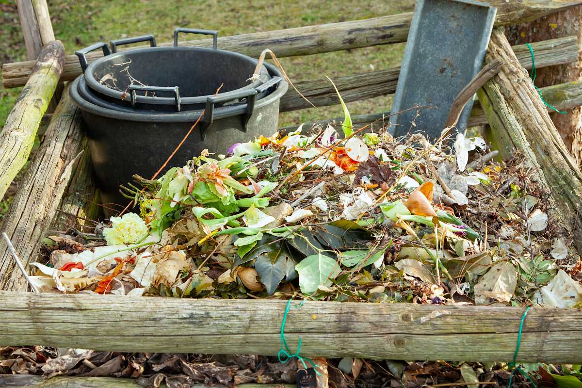 A wooden compost bin filled with various organic materials, including vegetable scraps, leaves, and garden waste.