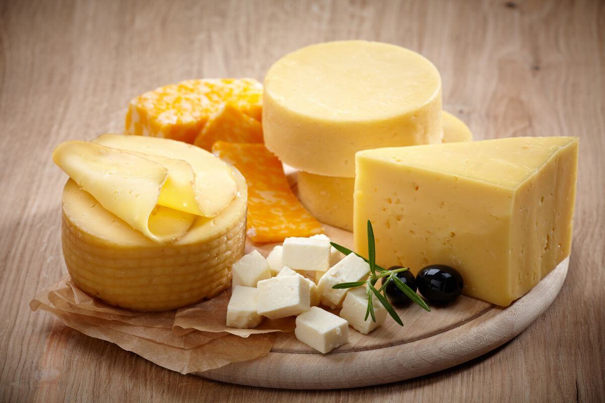 A wooden platter with various cheeses, including rounds, wedges, and cubes.