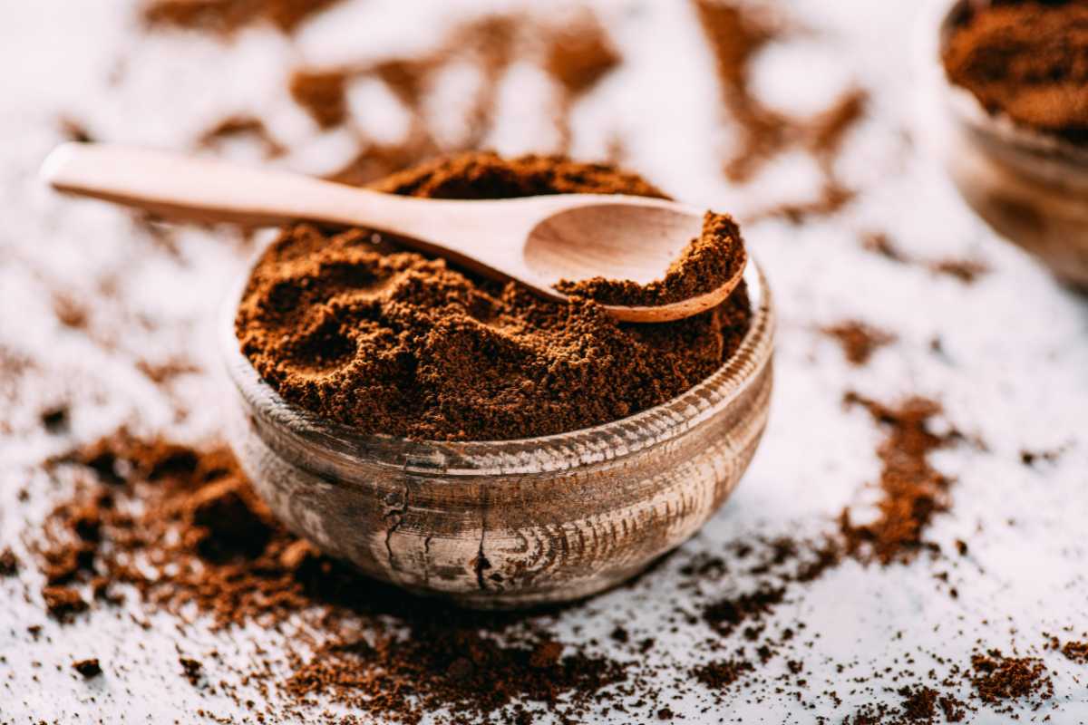 A wooden bowl filled with ground coffee, with a small wooden spoon resting on top. 