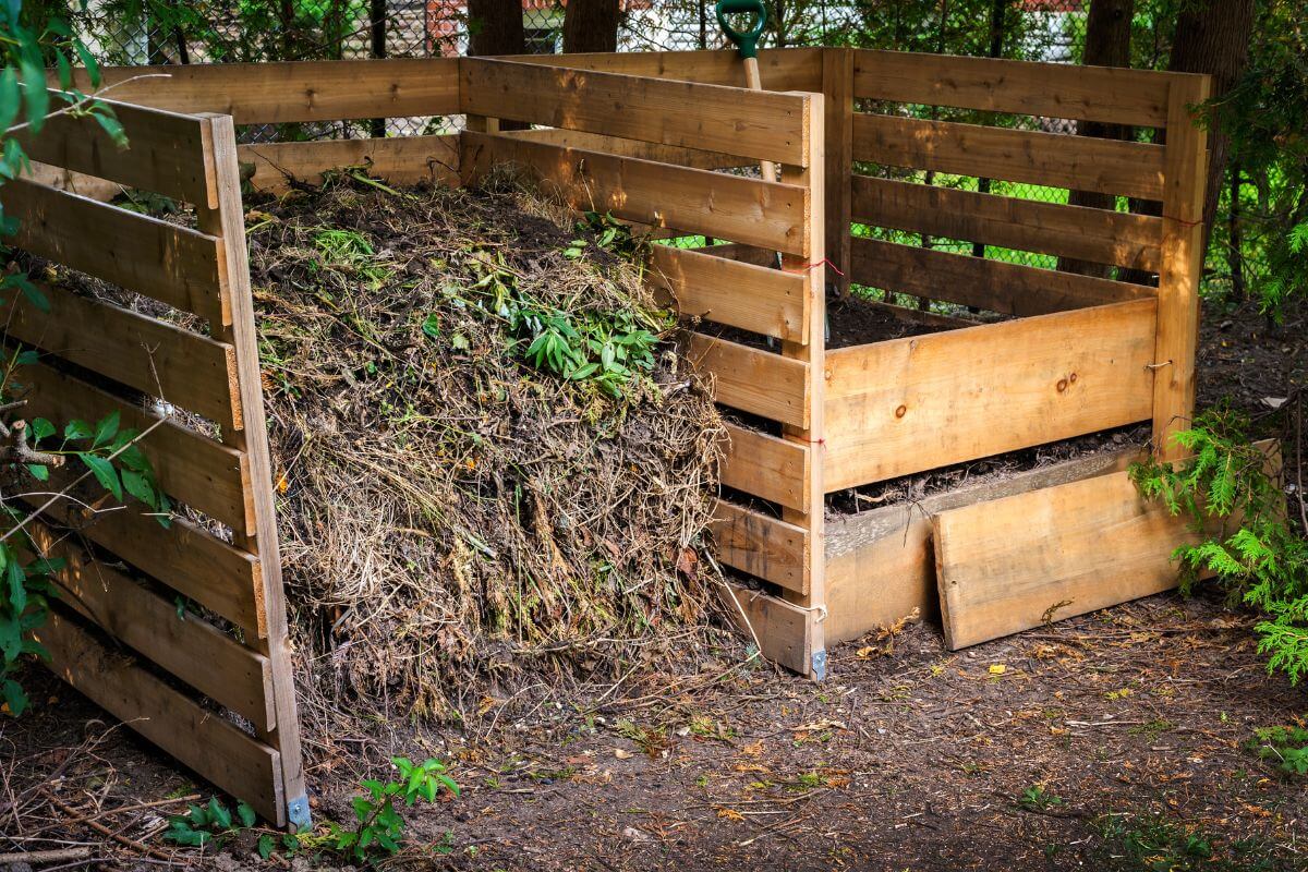 A wooden compost bin filled with garden waste, including leaves, branches, and other organic material.