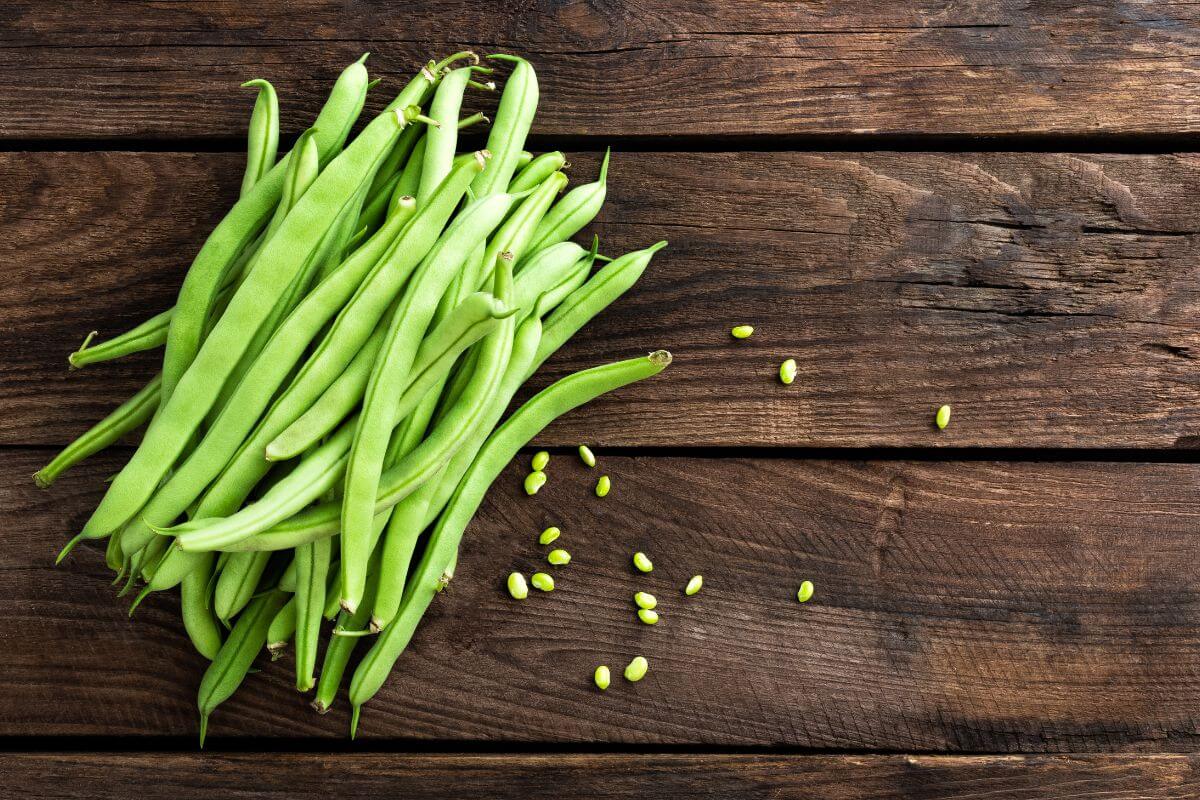 A bunch of green beans is laid out on a rustic wooden surface, with a few loose beans scattered near the pile. 
