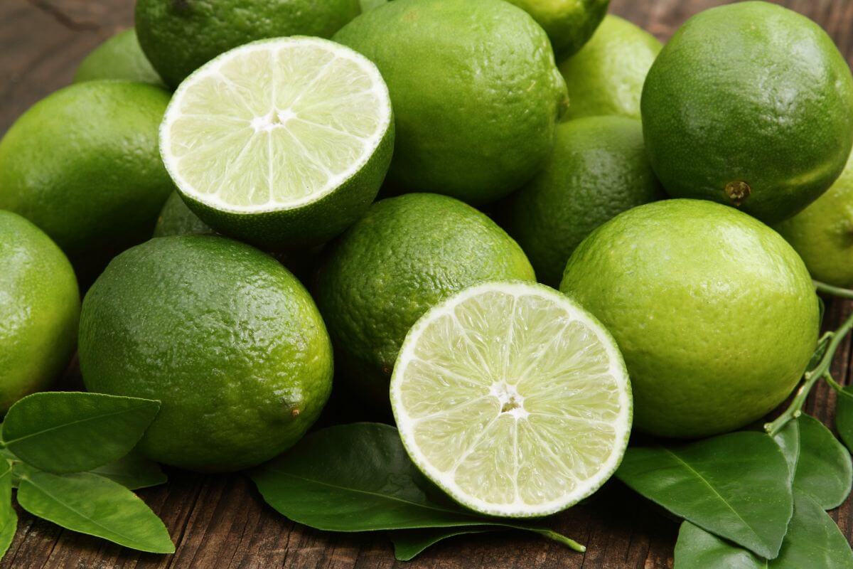 A pile of fresh green limes is displayed with one lime cut in half, revealing the juicy, segmented interior. 
