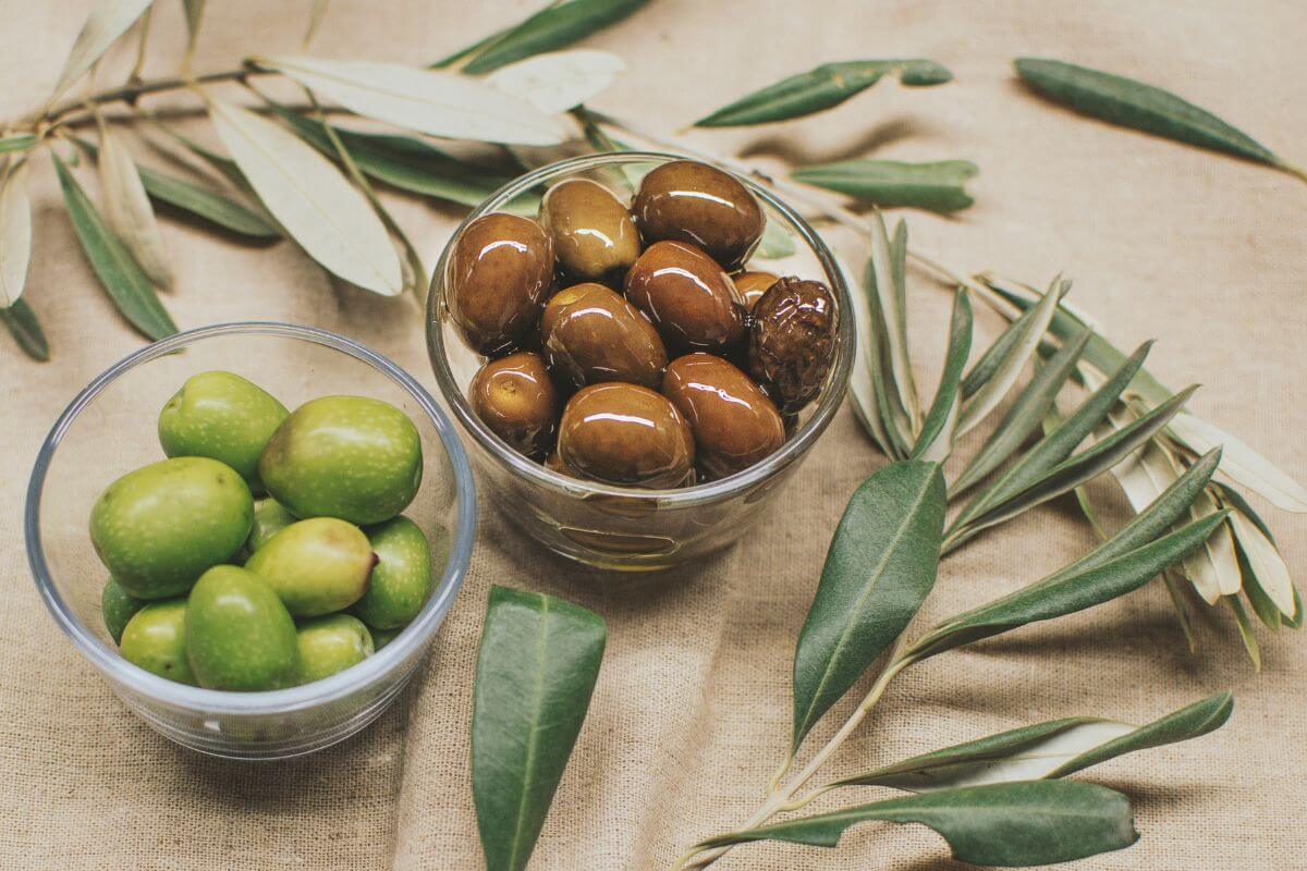 Two glass bowls filled with olives are placed on a fabric surface.