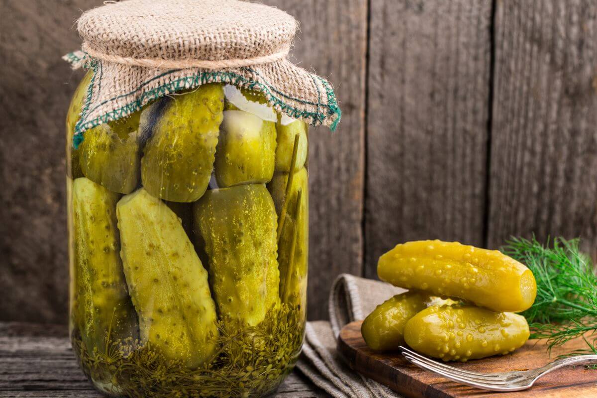 A glass jar filled with large pickles and herbs, sealed with a cloth cover. 