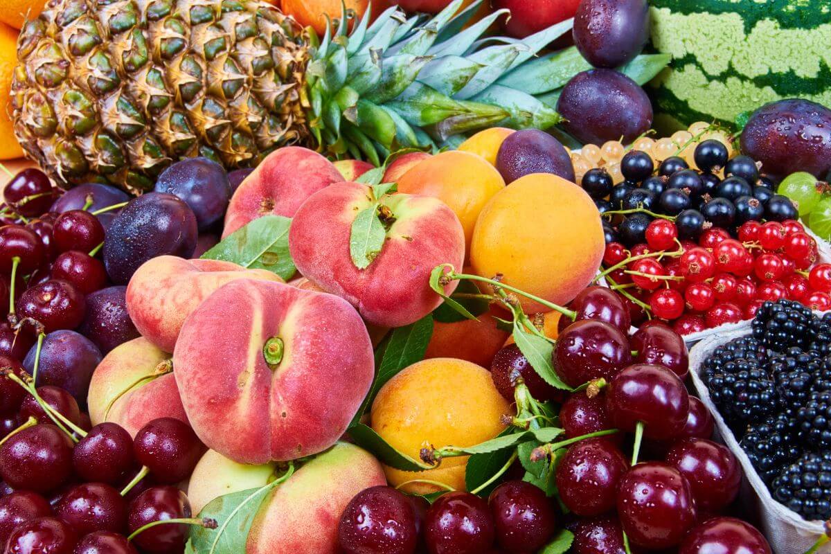A colorful assortment of fresh fruits including pineapples, peaches, cherries, apricots, blackberries, blueberries, and red currants.