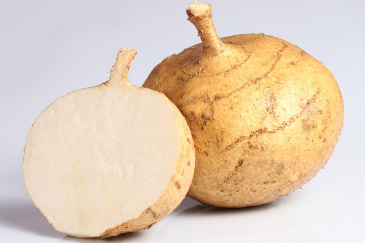 A whole jicama root with a rough, brown skin is placed beside a half-cut jicama, revealing its white, crisp, and juicy interior. 