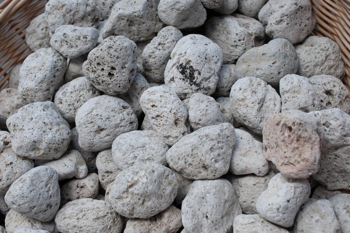 A close-up shot of a basket filled with many grey, irregularly shaped hydroponic pumice stones.