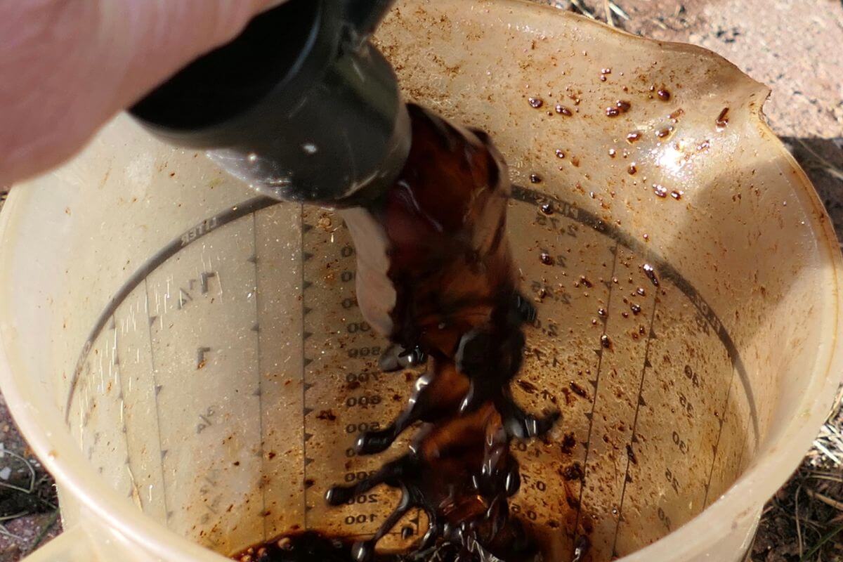 A hand holding a black container pour worm tea into a measuring cup with stained measurement markings.