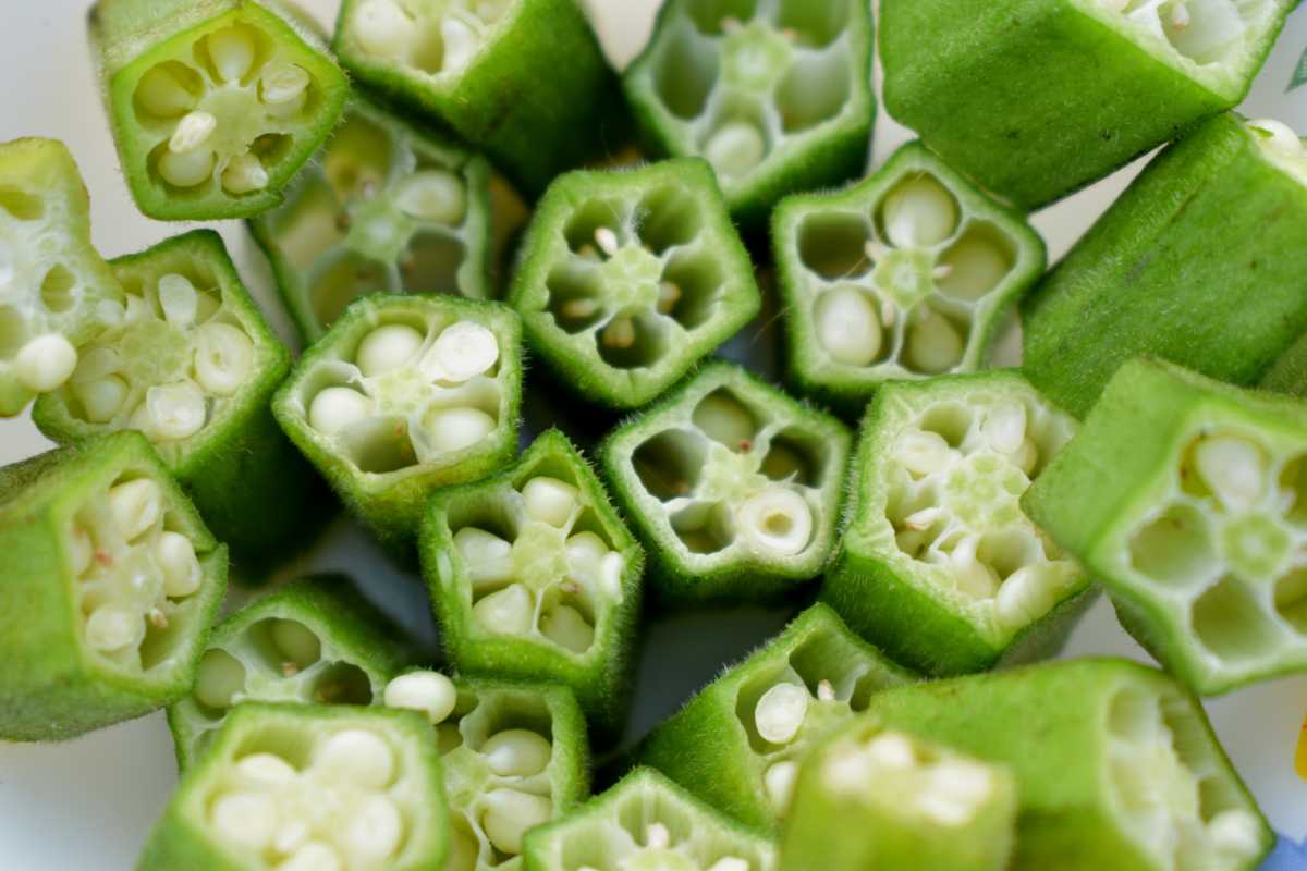 Freshly cut okra pieces. The green vegetable is sliced to reveal its unique interior with numerous seeds and star-shaped cross-sections.