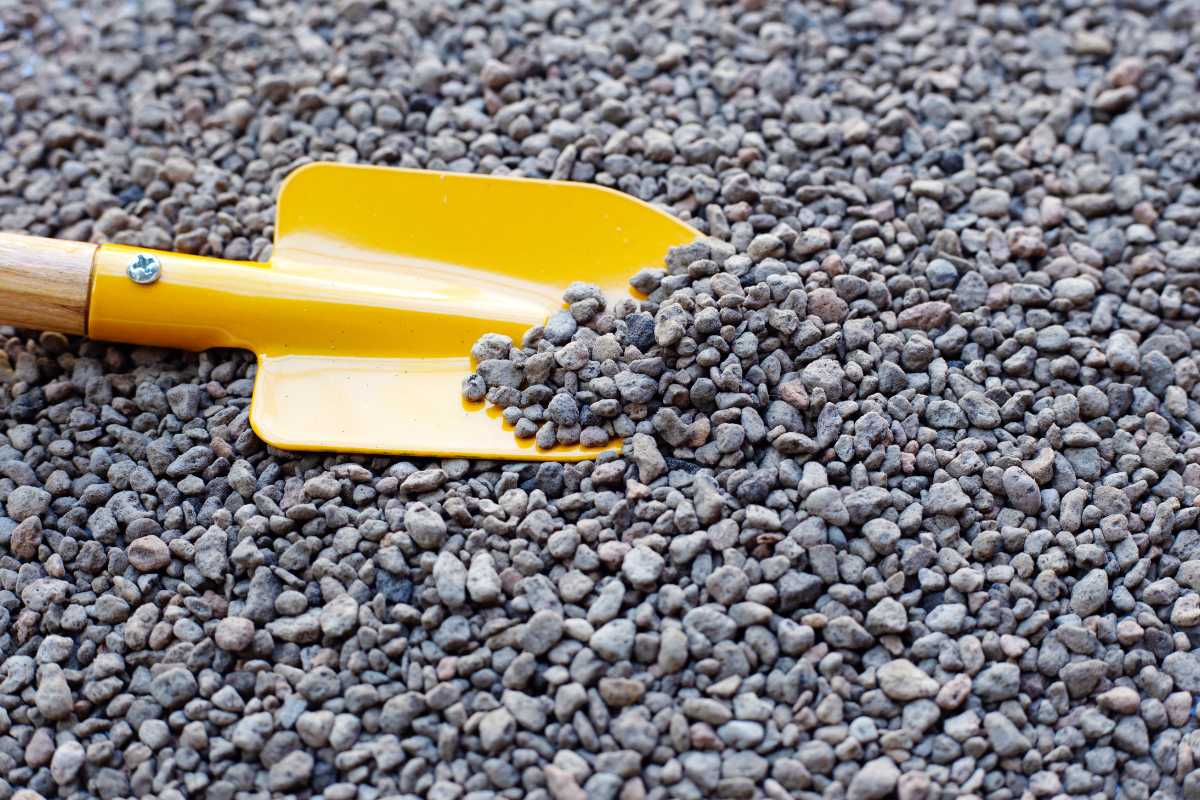 A small yellow shovel with a wooden handle lies on a surface covered in small, evenly spread pumice. 