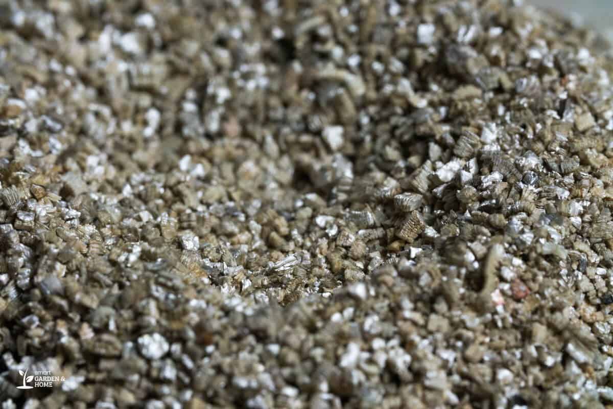 Close-up image of a heap of small, coarse vermiculite particles, displaying a mix of brownish-tan colors with occasional sparkles.