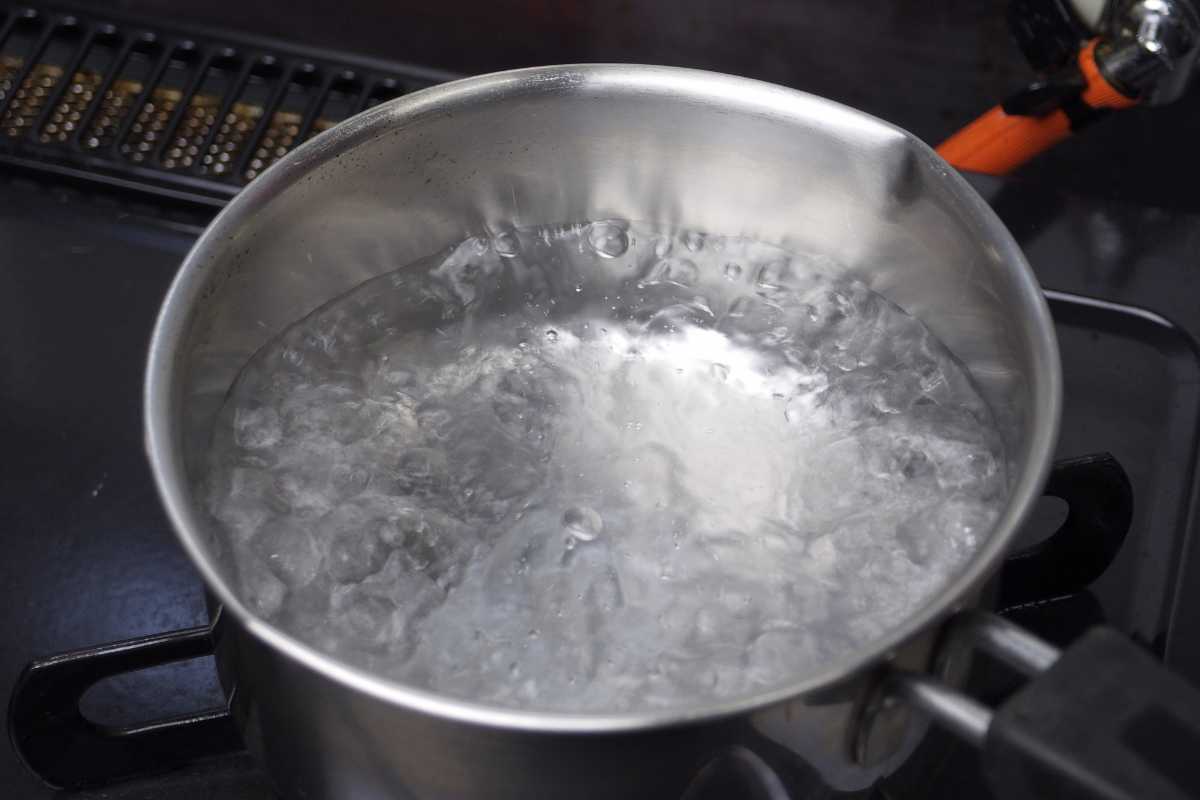 A pot of water is boiling on a stovetop. The water is bubbling vigorously, and steam is rising from the surface. 