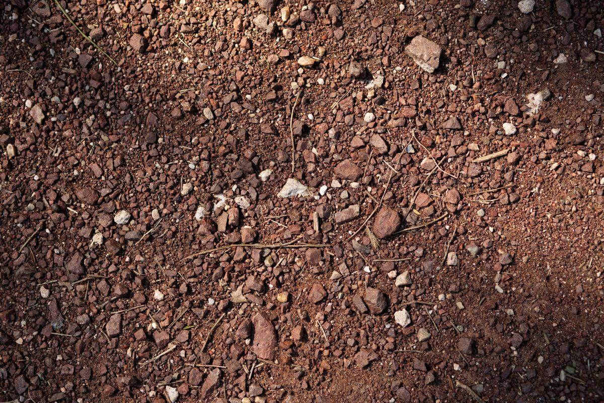 Close-up view of soil covered with small rocks, pebbles, and dirt with a reddish-brown hue.