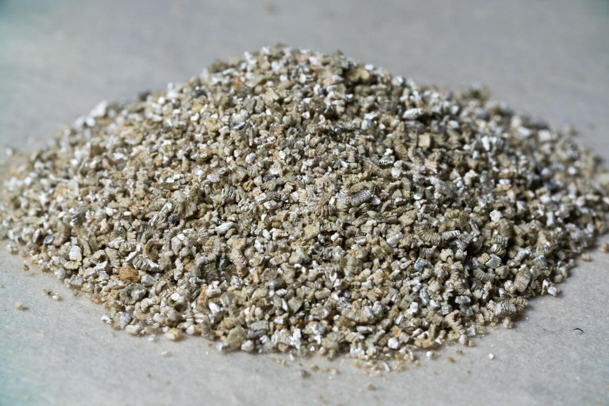 A close-up image of a small pile of beige and tan granules of vermiculite on a flat surface.