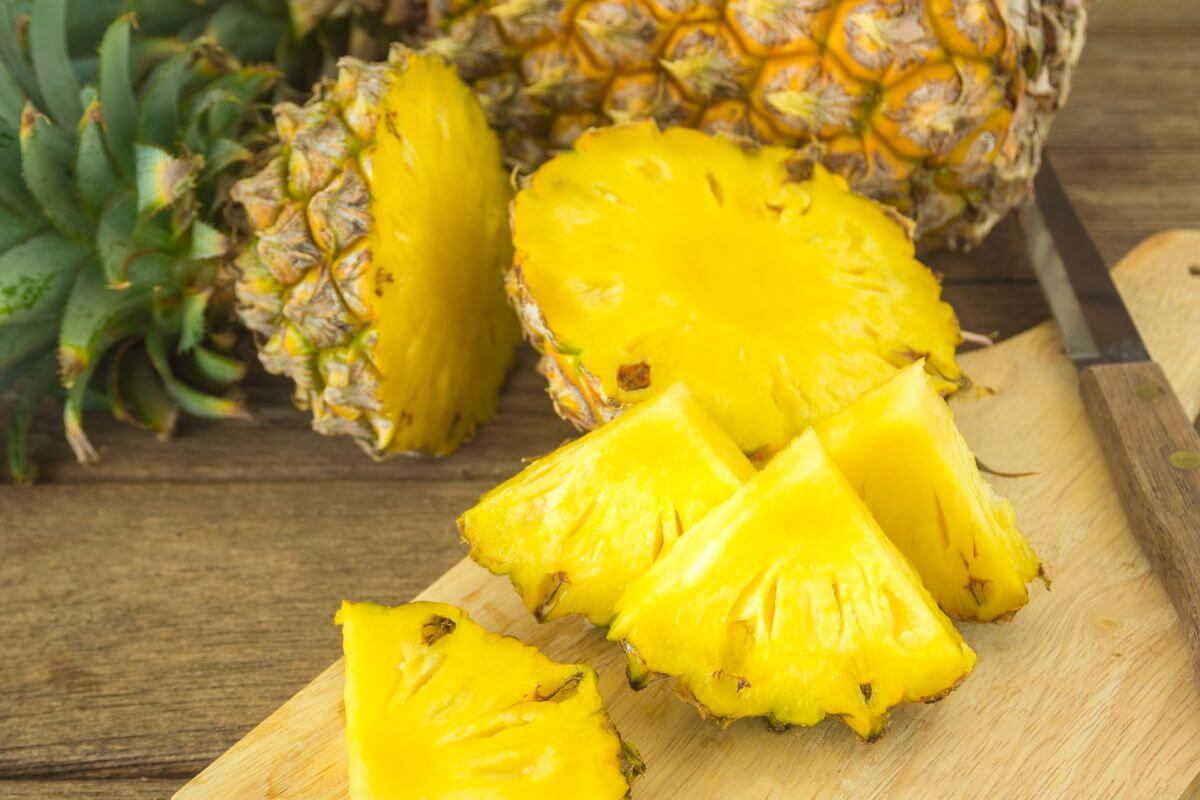 A ripe pineapple cut into several pieces on a wooden cutting board.