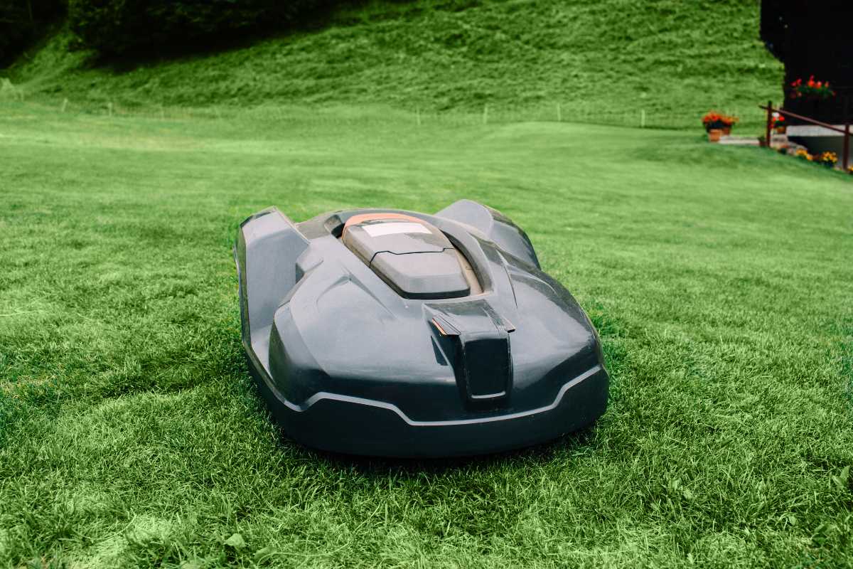 A sleek black robotic lawn mower autonomously trims a grassy lawn. 