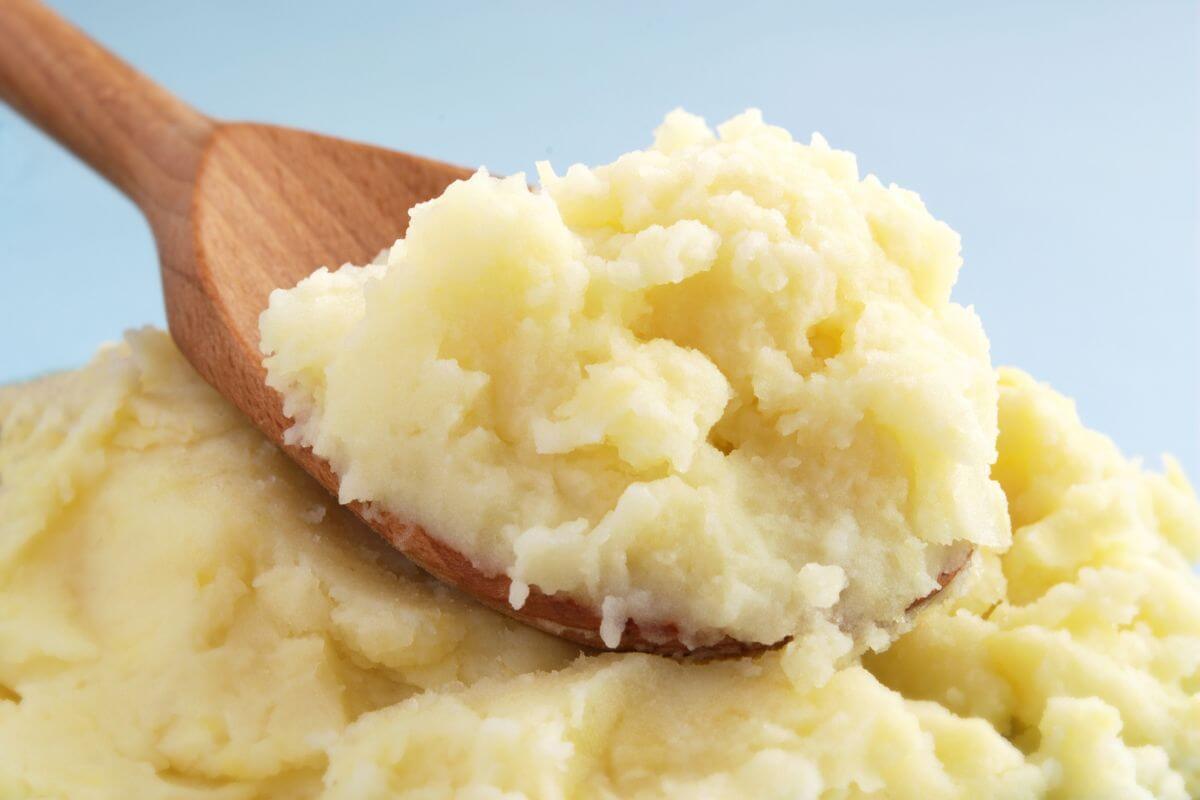 A close-up of creamy mashed potatoes being scooped with a wooden spoon.