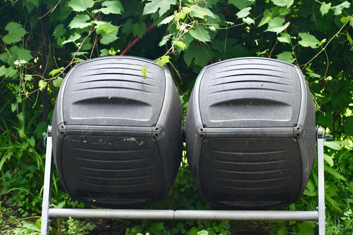 Two black compost tumbler bins made of plastic are mounted on a metal frame. 