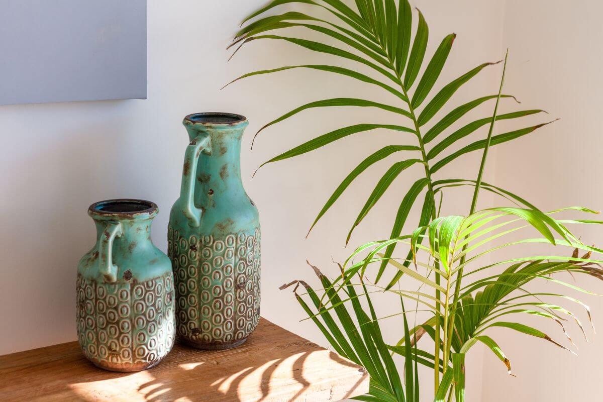 Two ceramic vases with blue and brown geometric patterns sit on a wooden surface next to a green majesty palm.