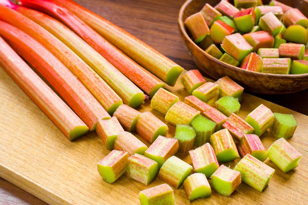 A wooden cutting board with long stalks of rhubarb, some of which are sliced into small cubes. 