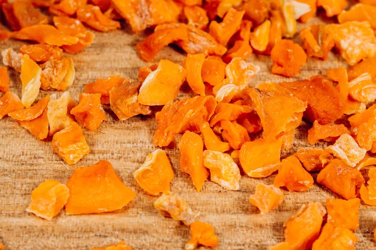 Scattered dried orange fruit pieces on a wooden surface. 