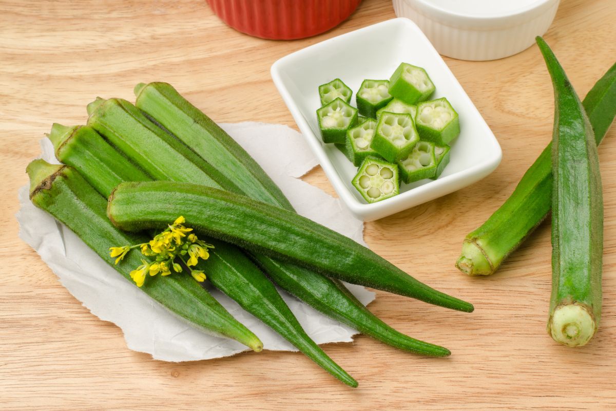 Okra pods arranged on a wooden surface with some cut pieces in a small white dish. 