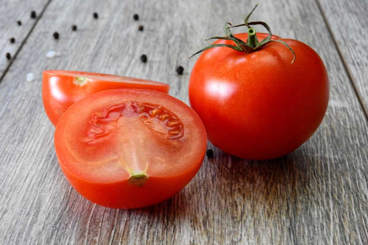 A whole red tomato and a sliced tomato with two halves are placed on a rustic wooden surface. 