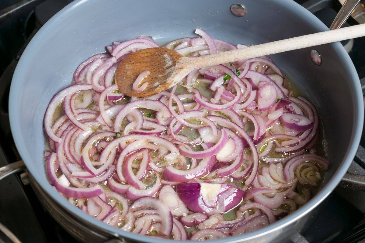 A saucepan filled with sliced red onions sautéing in oil.