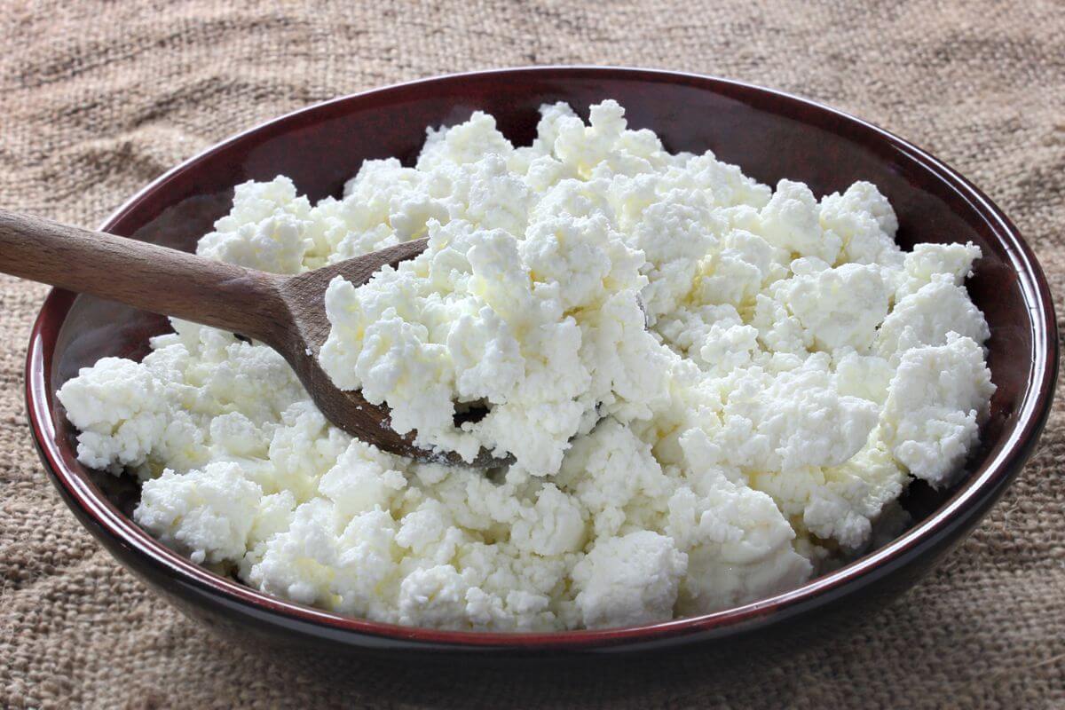 A dark brown bowl filled with cottage cheese is on a textured surface.