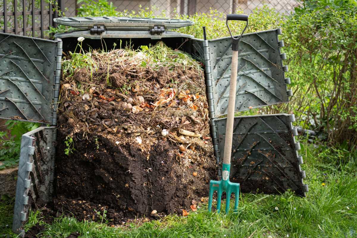 A compost bin filled with organic waste such as vegetable scraps and garden clippings is open, revealing its contents. 