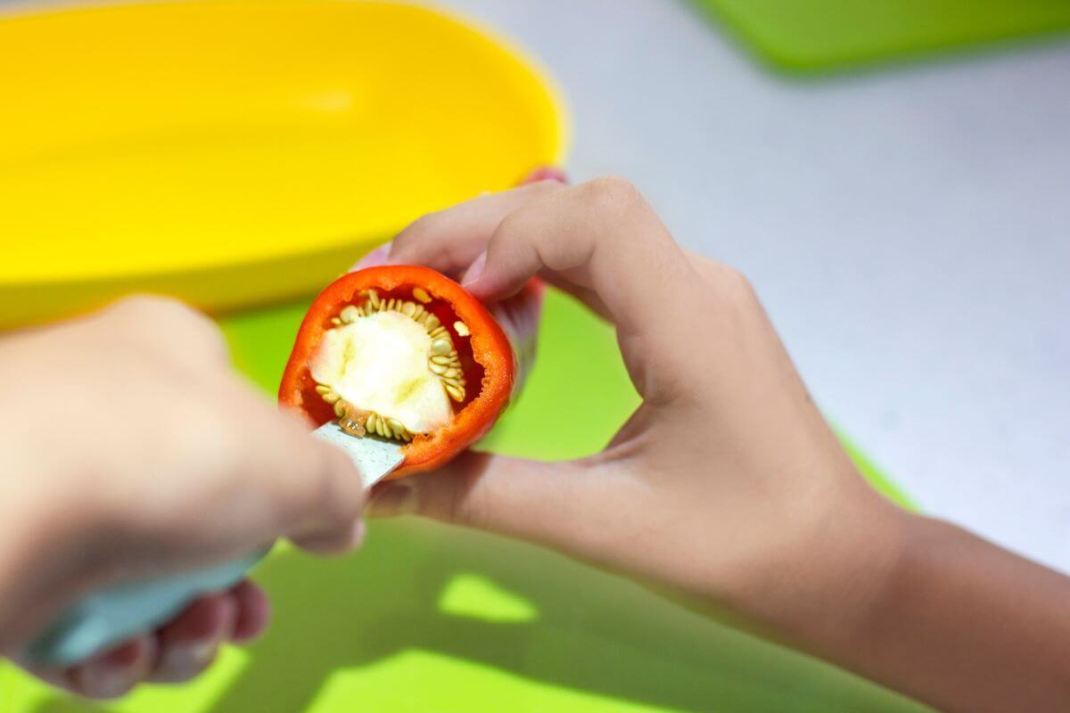 A person is holding a red bell pepper and using a white knife to remove the seeds and white membrane from the inside.