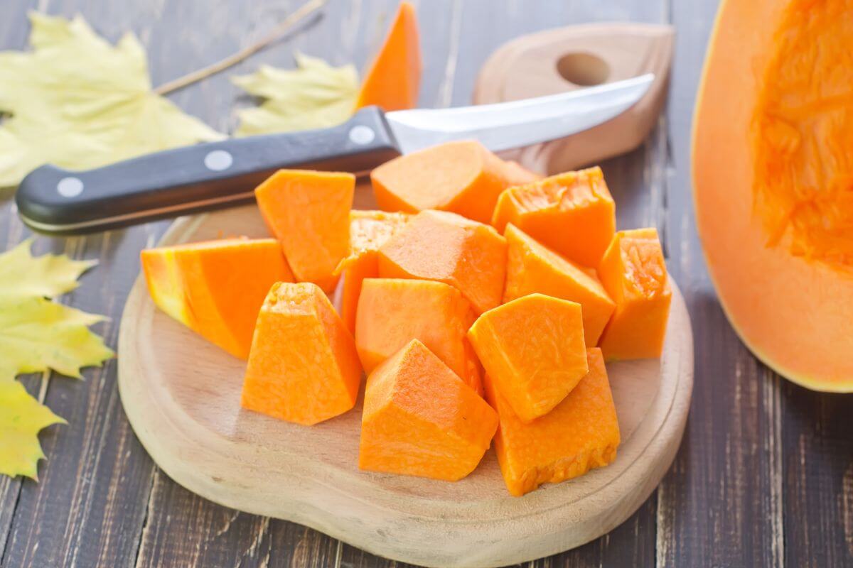 Cubed pieces of pumpkin on a wooden cutting board with a knife beside them.