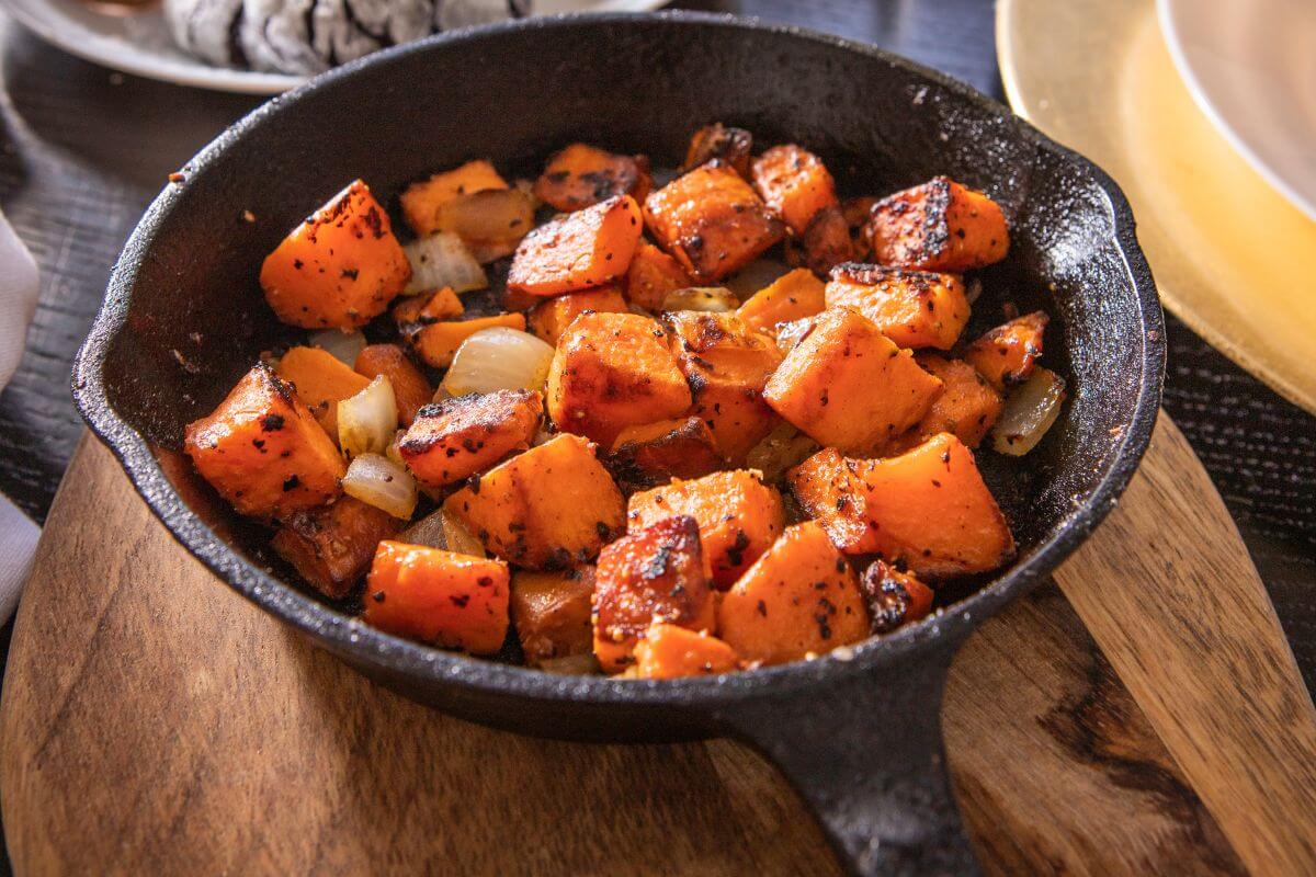 A cast-iron skillet filled with roasted sweet potato and onion chunks, seasoned and browned.