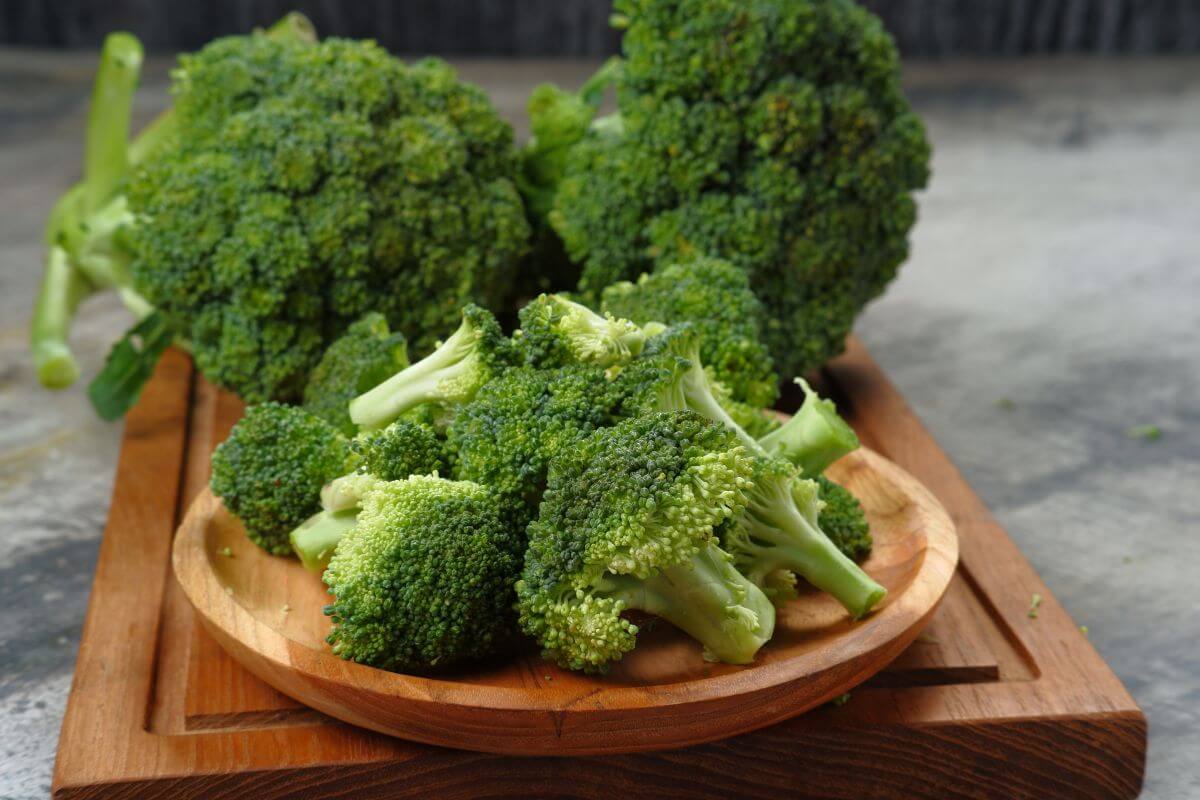 A wooden platter filled with fresh broccoli florets on a wooden chopping board.