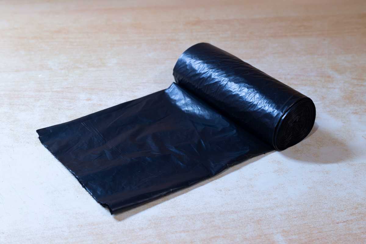 A partially unrolled black plastic garbage bag roll placed on a light wooden surface. 