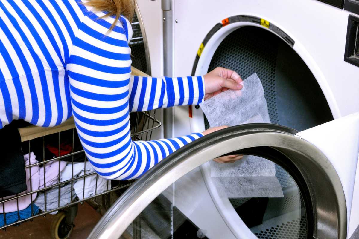 A person wearing a blue and white striped top is placing a dryer sheet into a front-loading dryer. 