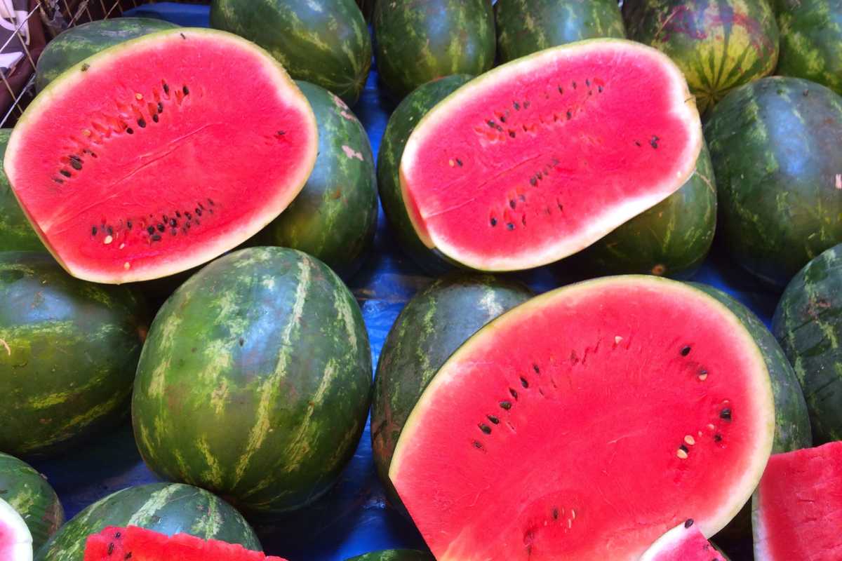 A display of watermelons, some whole and some cut in half, showcasing their vibrant red interior and black seeds, is placed on a blue surface. 