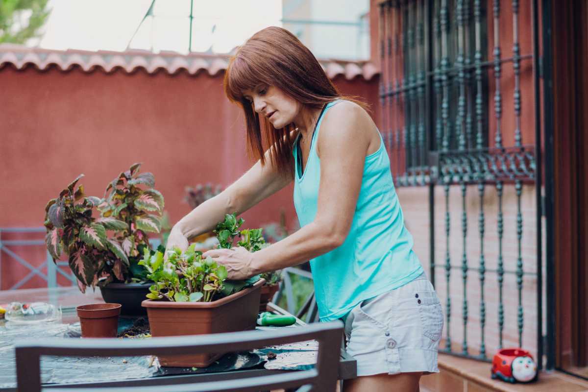 A woman with long, reddish-brown hair is gardening on a patio. 