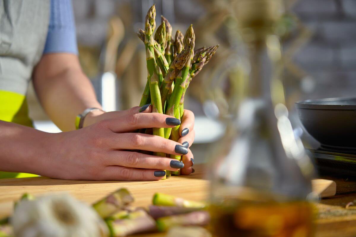 A person is holding a bunch of fresh asparagus over a wooden cutting board.