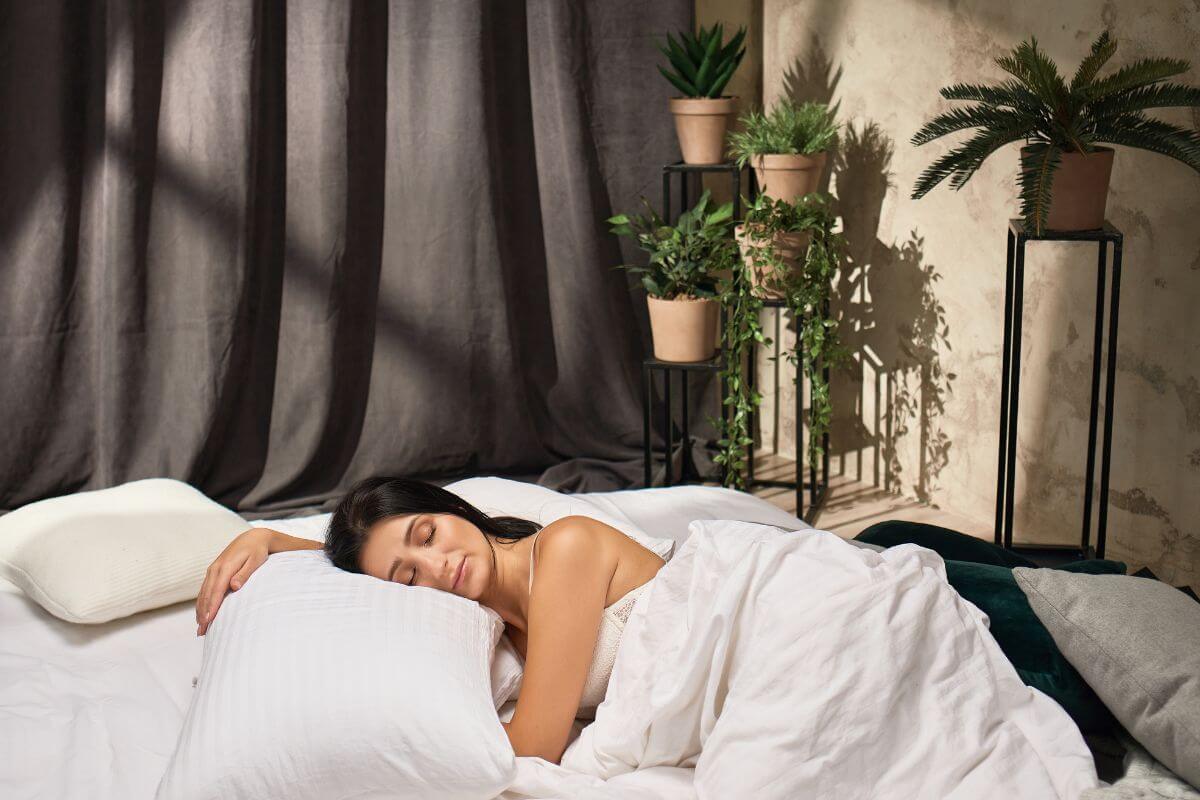 A woman peacefully sleeping in a bed, surrounded by several potted plants on stands against the wall.