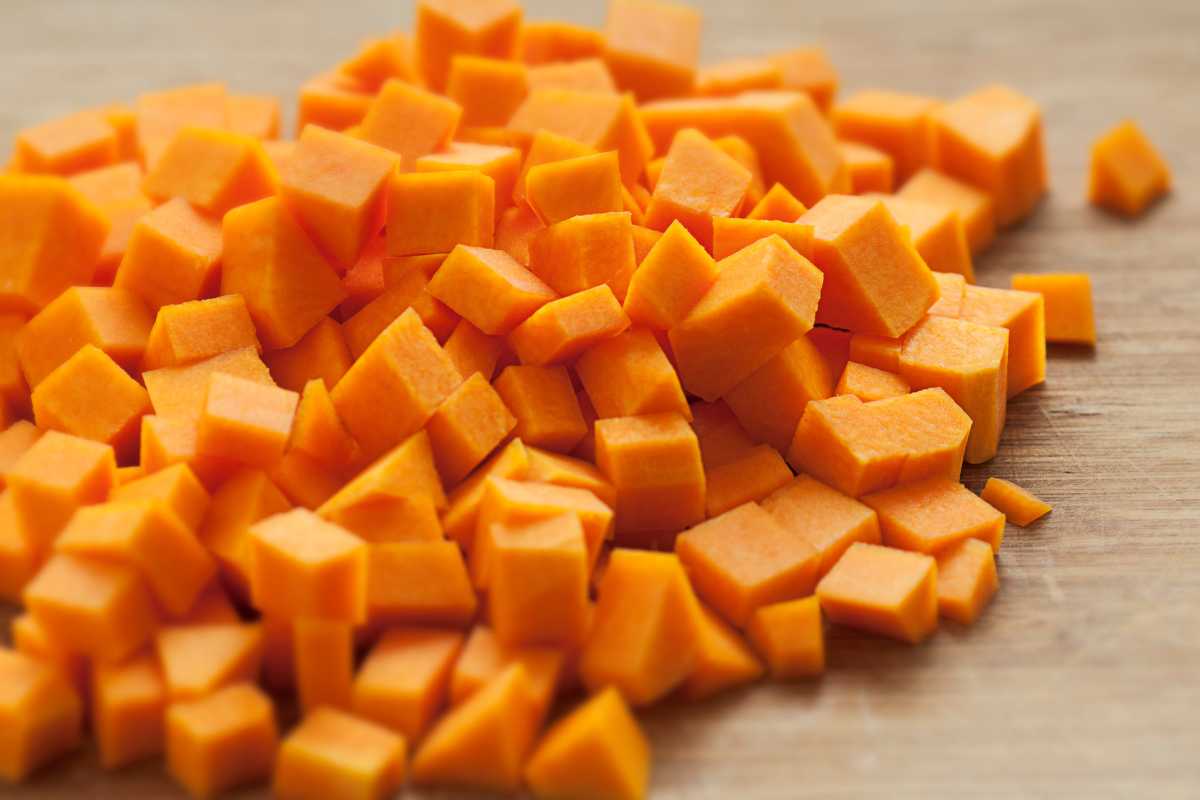 A pile of diced orange squash on a wooden surface. The carrot pieces are evenly cut into small cubes.