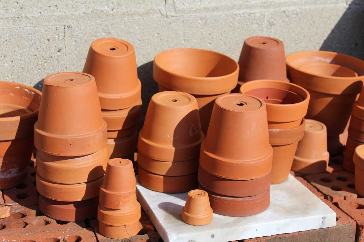 A collection of various-sized terracotta plant pots is stacked on a brick and marble surface. 