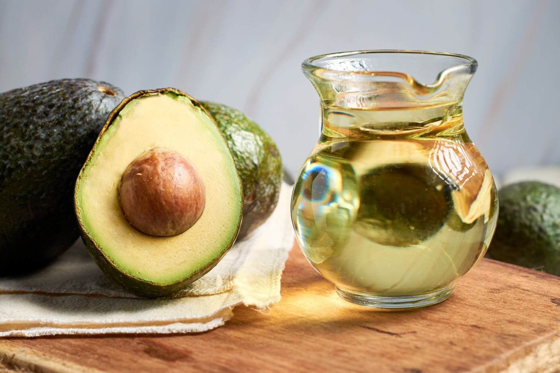 A glass jar filled with clear avocado oil sits on a wooden surface next to a halved avocado.