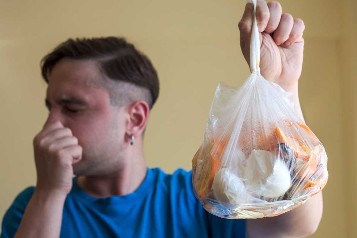 A person in a blue shirt is holding a clear plastic bag filled with trash and organic waste.