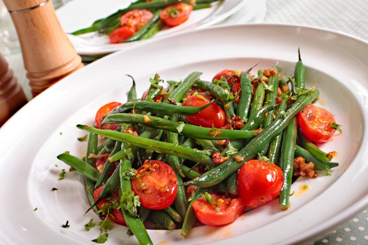A white plate filled with a green bean and cherry tomato salad, garnished with chopped herbs and a light dressing.