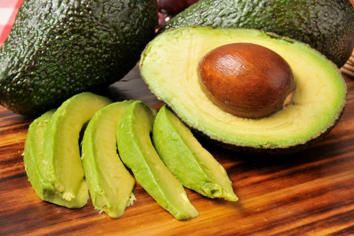 A ripe hydroponic avocado cut in half exposing the pit is placed on a wooden cutting board.