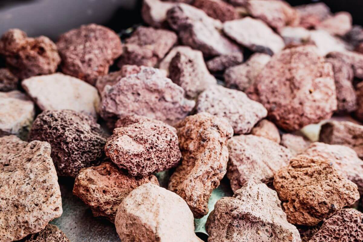 A close-up shot of several tan, reddish, and beige lava rocks, varying in texture and size, scattered in an outdoor setting.