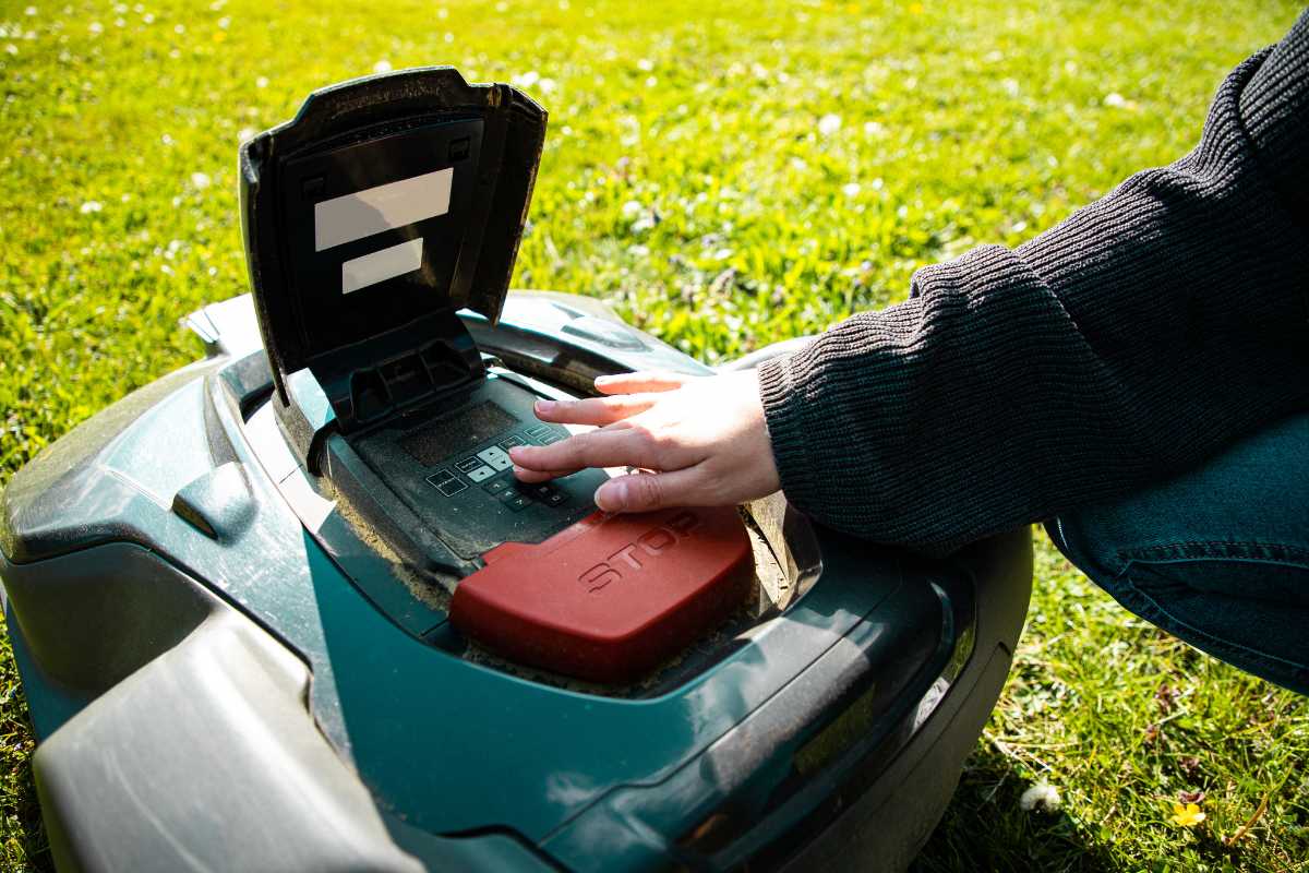 A person wearing a dark long-sleeved shirt is programming a robotic lawn mower.