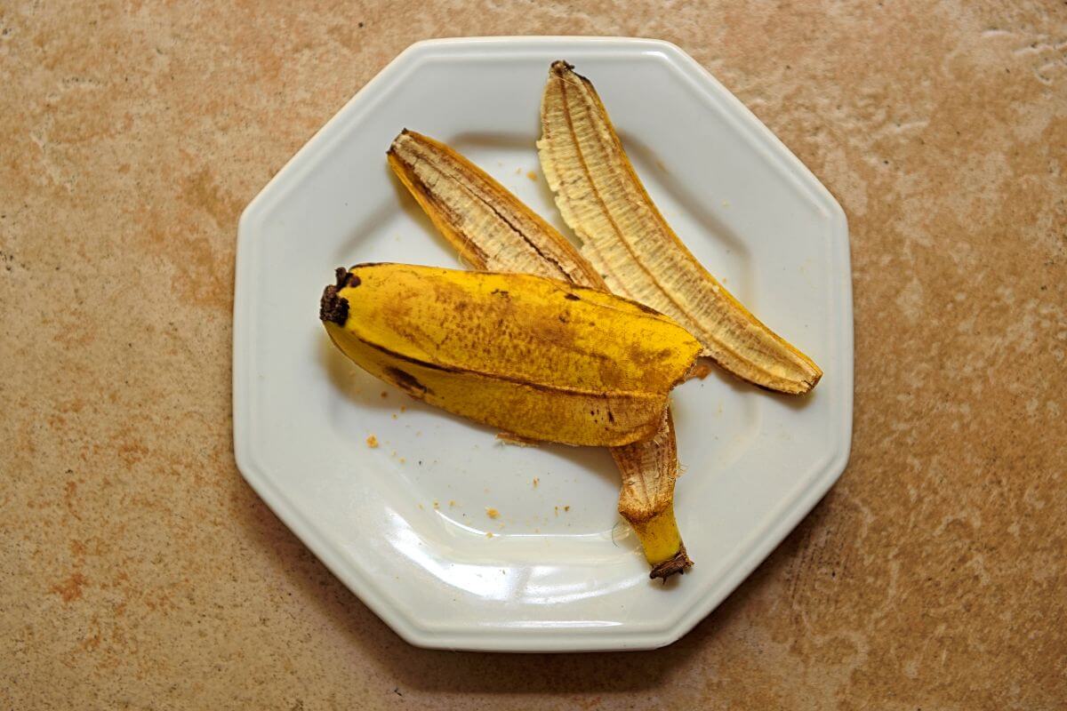 A partially peeled banana with some of its peel pieces resting beside it on a white, octagonal plate.